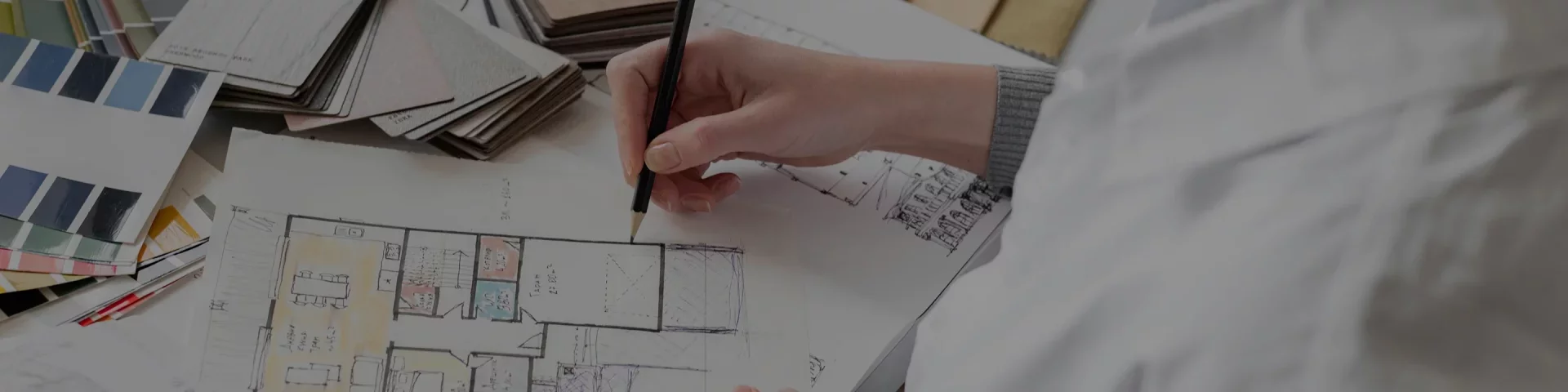 Person sketching a colored architectural floor plan with paint color swatches nearby.